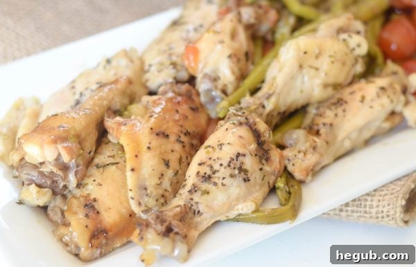 Close-up of Slow Cooker Lemon Pepper Chicken and Veggies, showing the crispy skin of the chicken wings and the vibrant colors of asparagus and tomatoes.