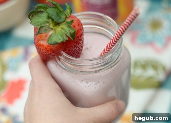 A blended strawberry smoothie in a glass, with fresh strawberries, next to a mason jar of prepped ingredients
