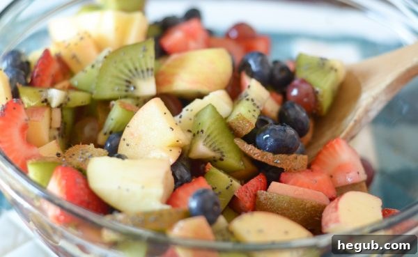 Effortless Poppy Seed Fruit Medley 5 Hands mixing a large bowl of colorful fruits for the Poppy Seed Fruit Salad, with a lime half and honey nearby. The scene conveys freshness and the start of a healthy preparation.