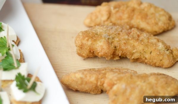 Preparing Parmesan Herb Bites: Tyson Chicken Strips being sliced, ready to be paired with cheese and parsley for a holiday appetizer.