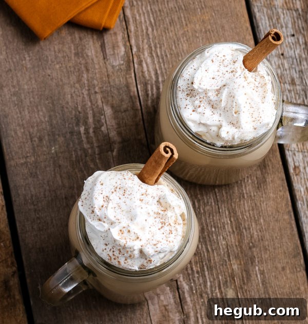 Two mugs of homemade Pumpkin Spice Latte, one topped with whipped cream, set on a wooden table with fall decorations.